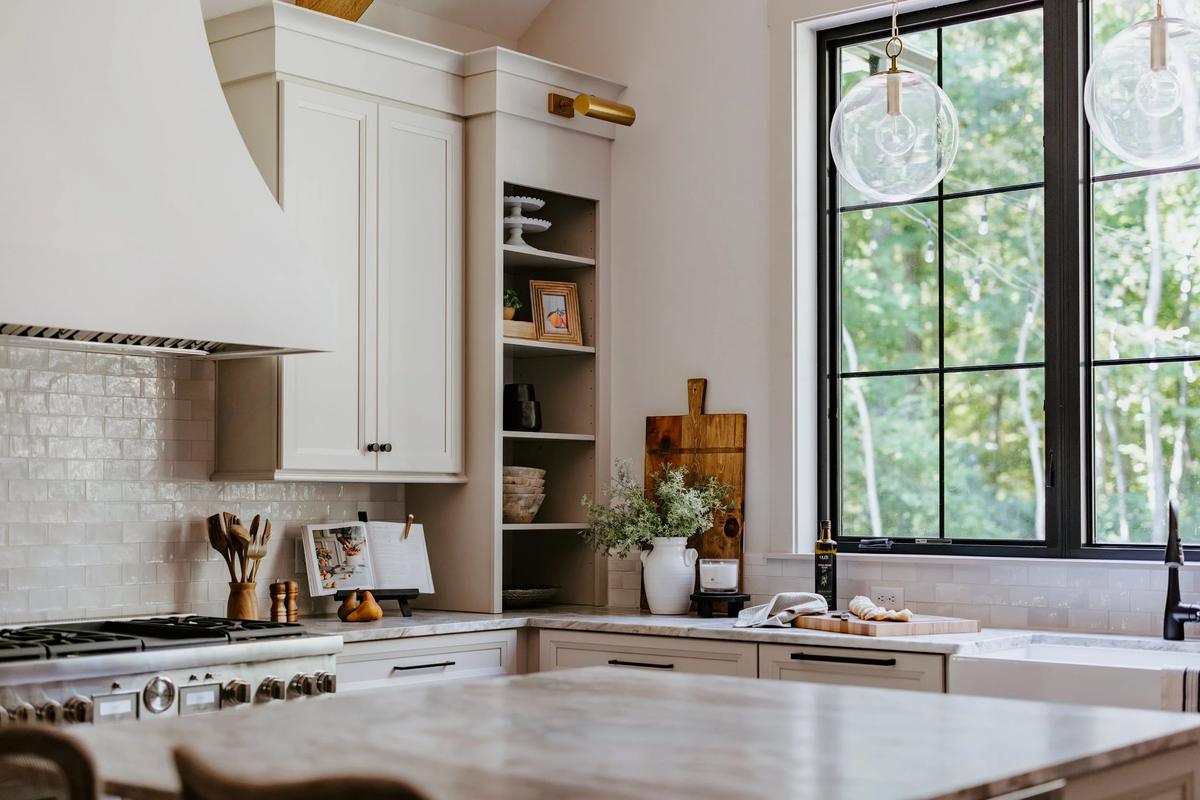 Kitchen with white cabinets, a large black window, hanging glass pendant lights, and a marble countertop with decorative items and plants.