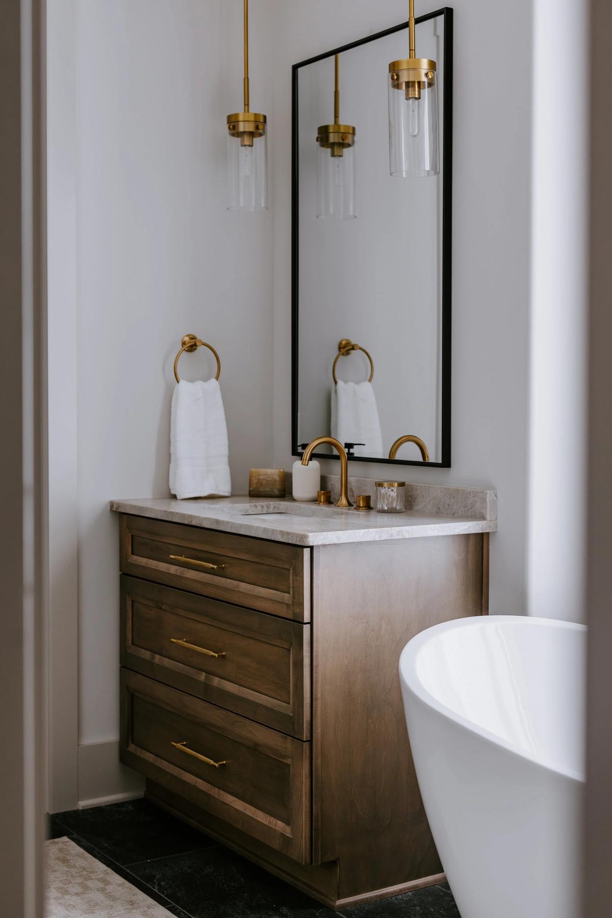 Modern bathroom with wooden vanity, marble countertop, gold fixtures, a large mirror, and hanging pendant lights.