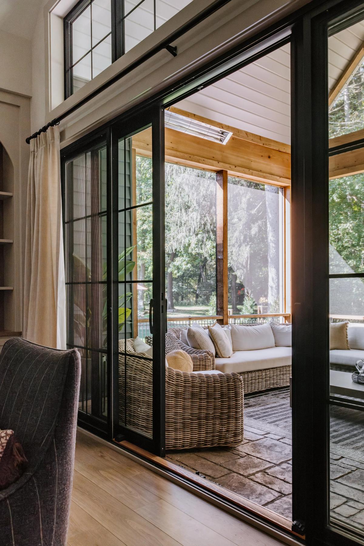 A view through a sliding glass door into a screened porch with outdoor furniture and trees outside.